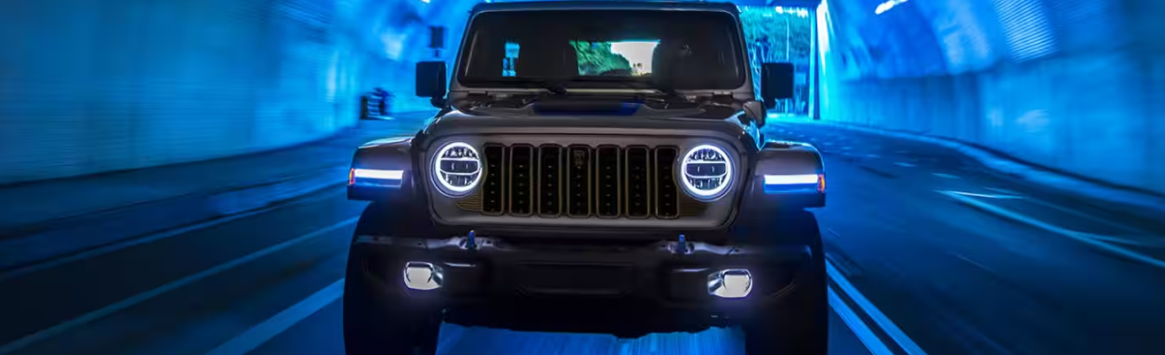 A black Jeep Wrangler 4xe drives through a brightly lit tunnel with blue accents.